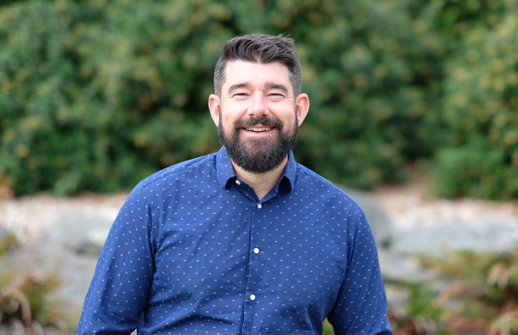 John Scott smiling outdoors in a blue shirt